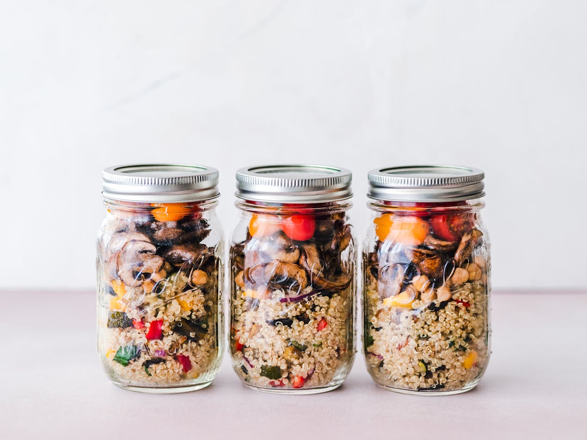 Três potes de vidro com saladas e grãos preparados para a semana