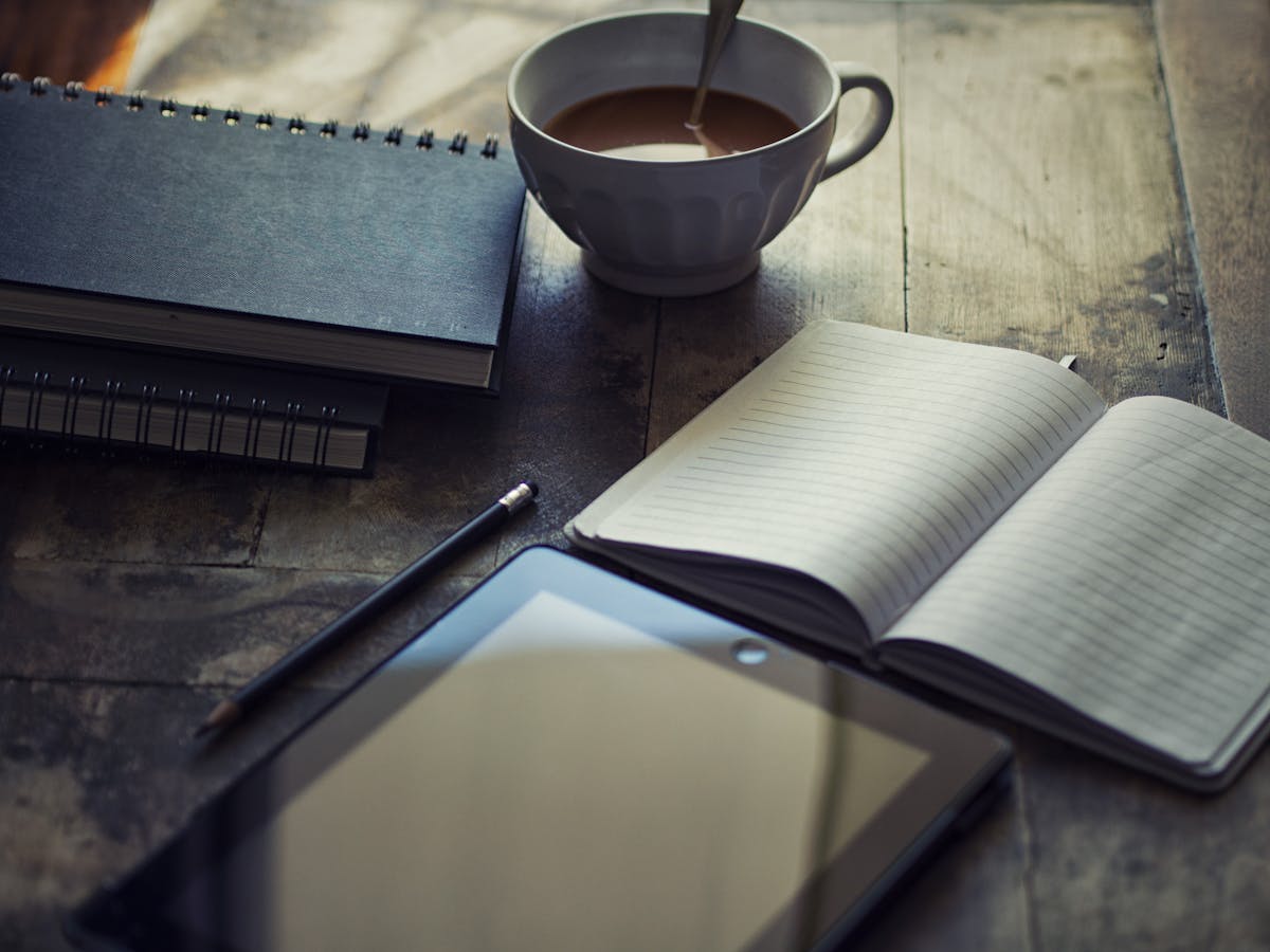 Xícara de café ao lado de um caderno aberto sobre a mesa
