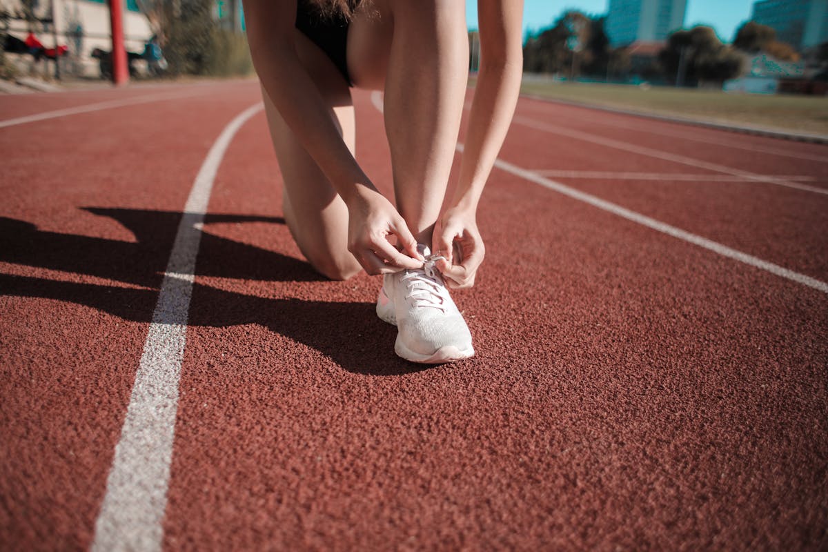 Mulher amarrando o tênis em uma pista, pronta para começar a se exercitar