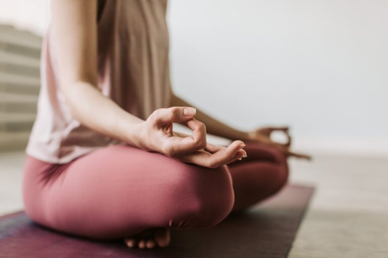 Mulher sentada de olhos fechados meditando em ambiente tranquilo