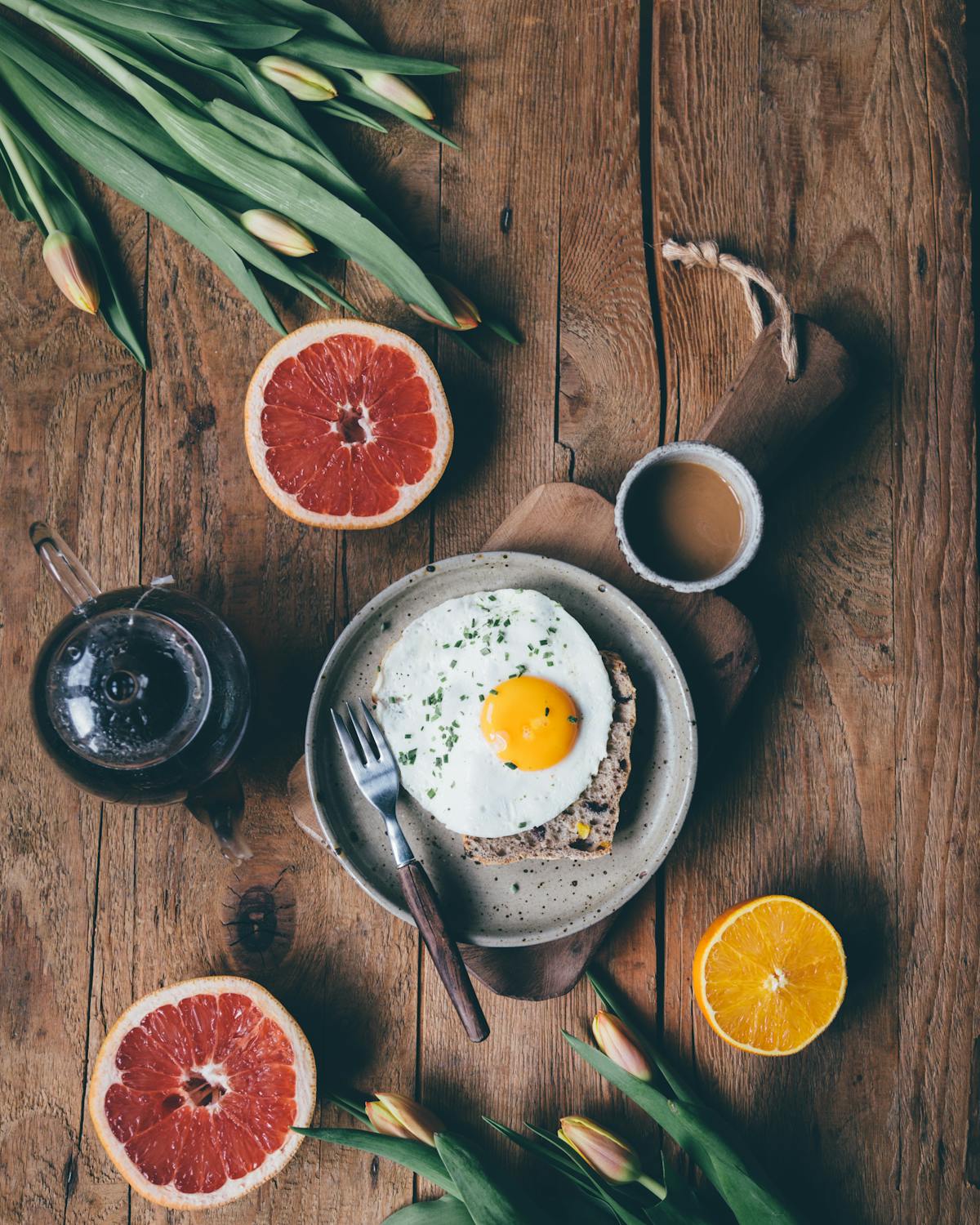 Mesa de madeira com café da manhã: ovo, frutas cítricas, pão e café