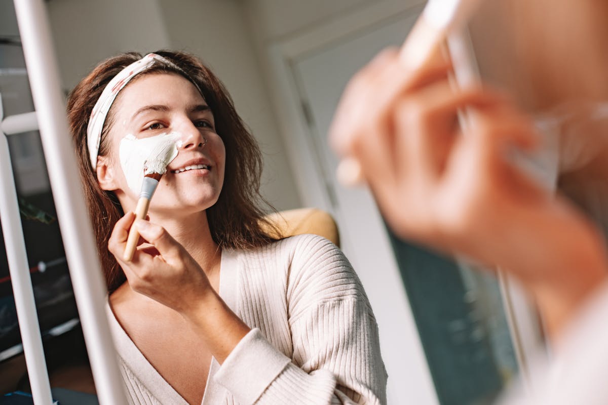 Mulher diante do espelho aplicando máscara facial em momento de autocuidado