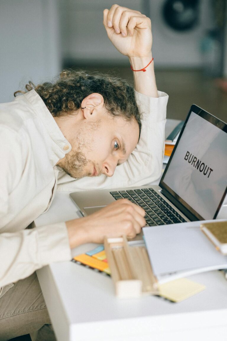 Pessoa deitada sobre a mesa em frente ao laptop, adiando o trabalho