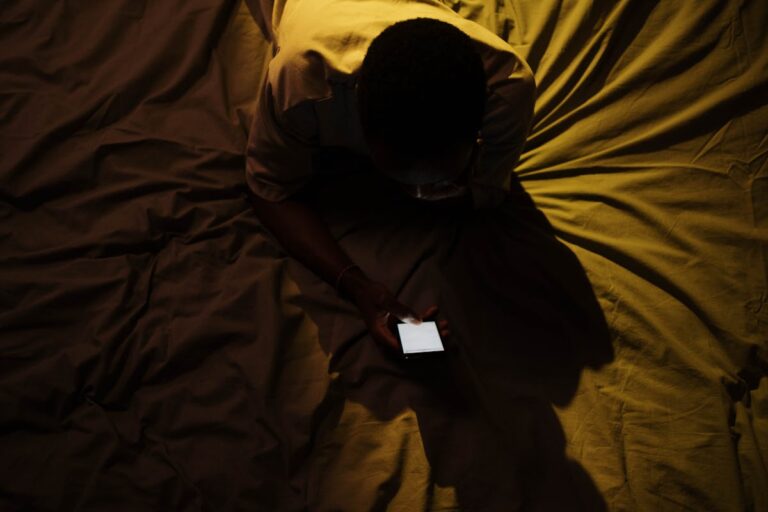 Homem deitado na cama acordado usando o celular durante a noite