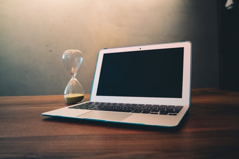 Laptop ao lado de uma ampulheta sobre mesa de madeira