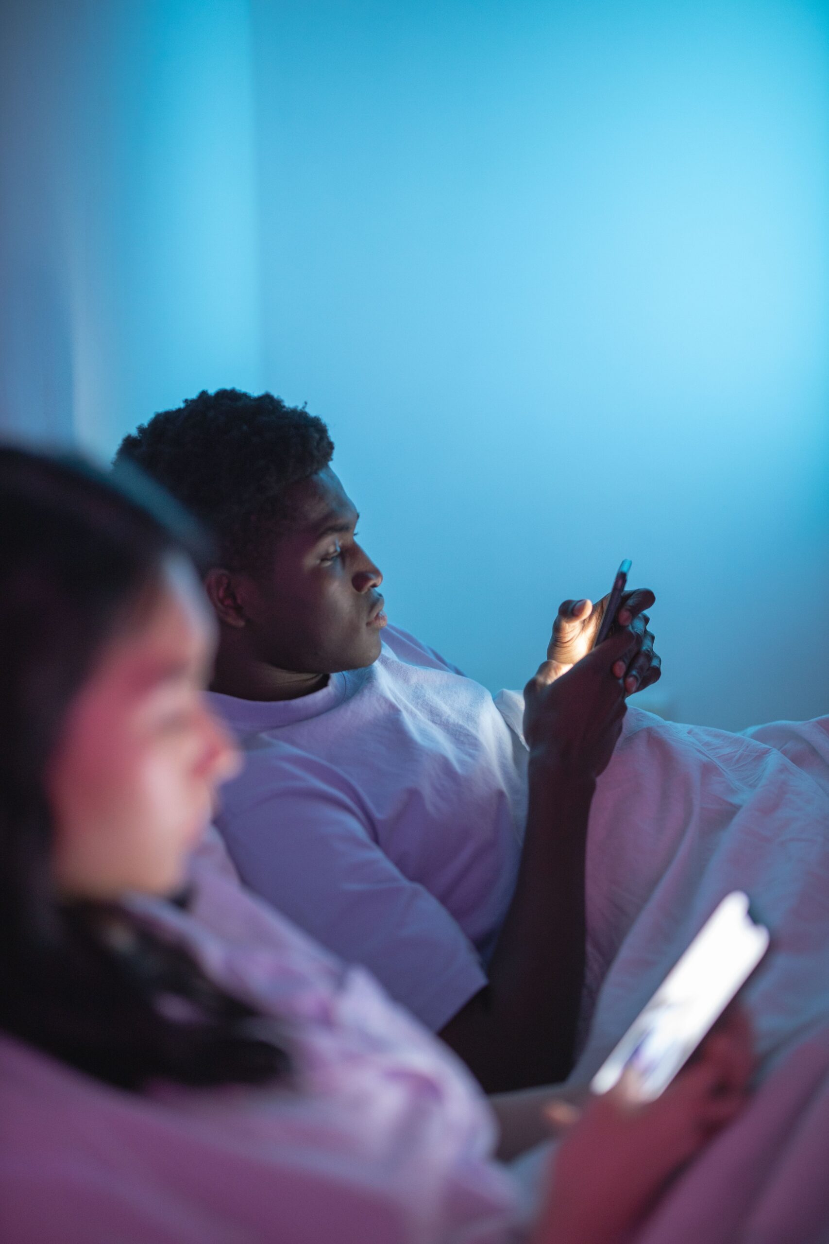 Casal na cama à noite com o rosto iluminado pela luz azul dos celulares