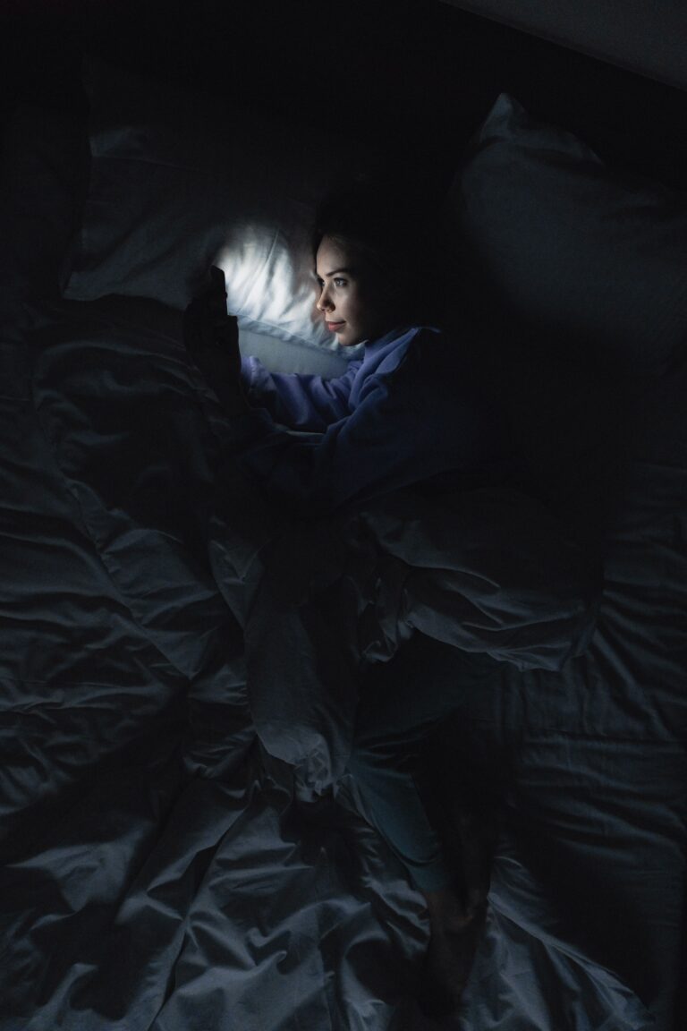 Mulher deitada na cama à noite usando o celular, com o rosto iluminado pela tela
