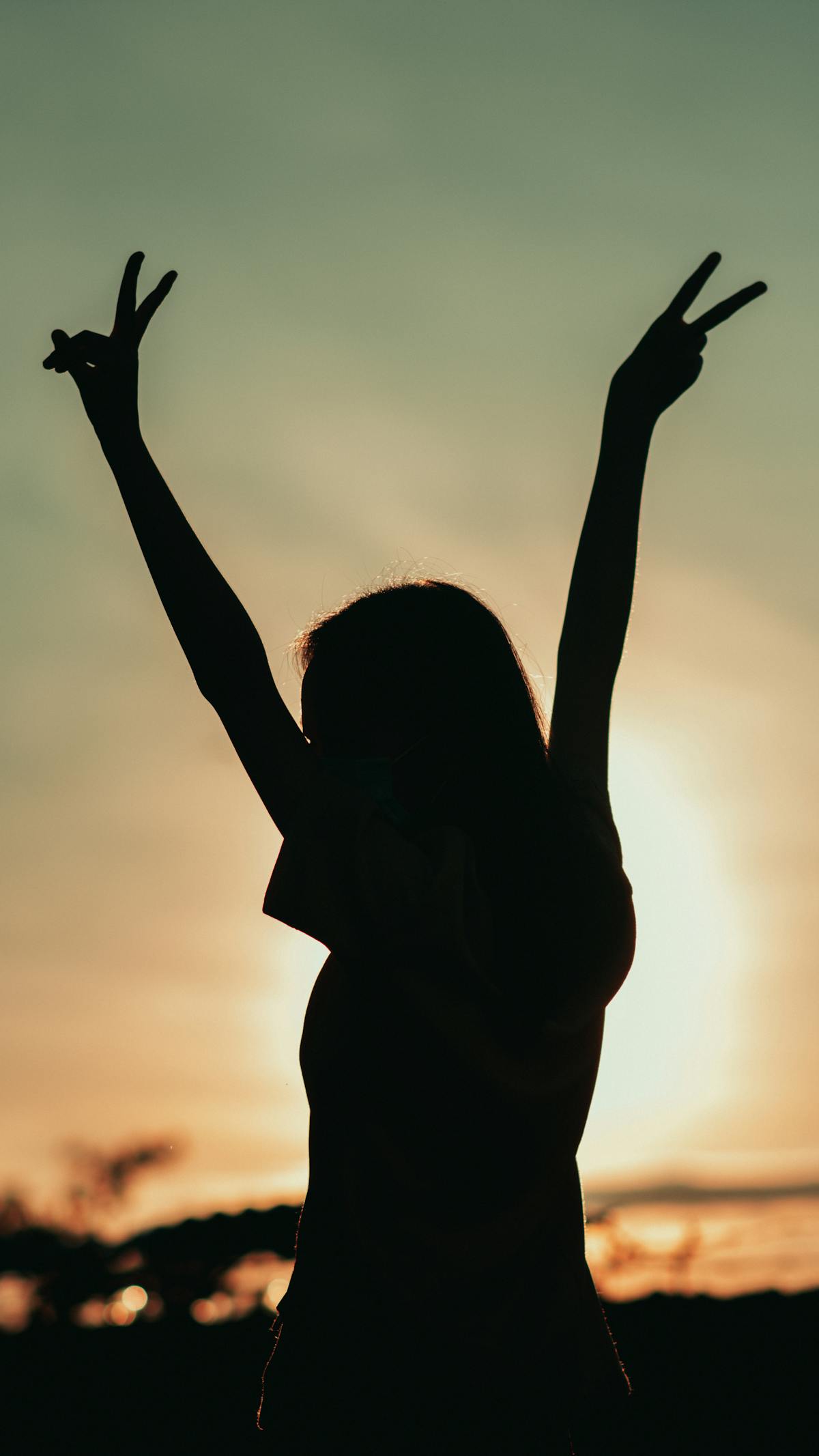 Silhueta de mulher erguendo os braços ao entardecer, sensação de liberdade e gratidão