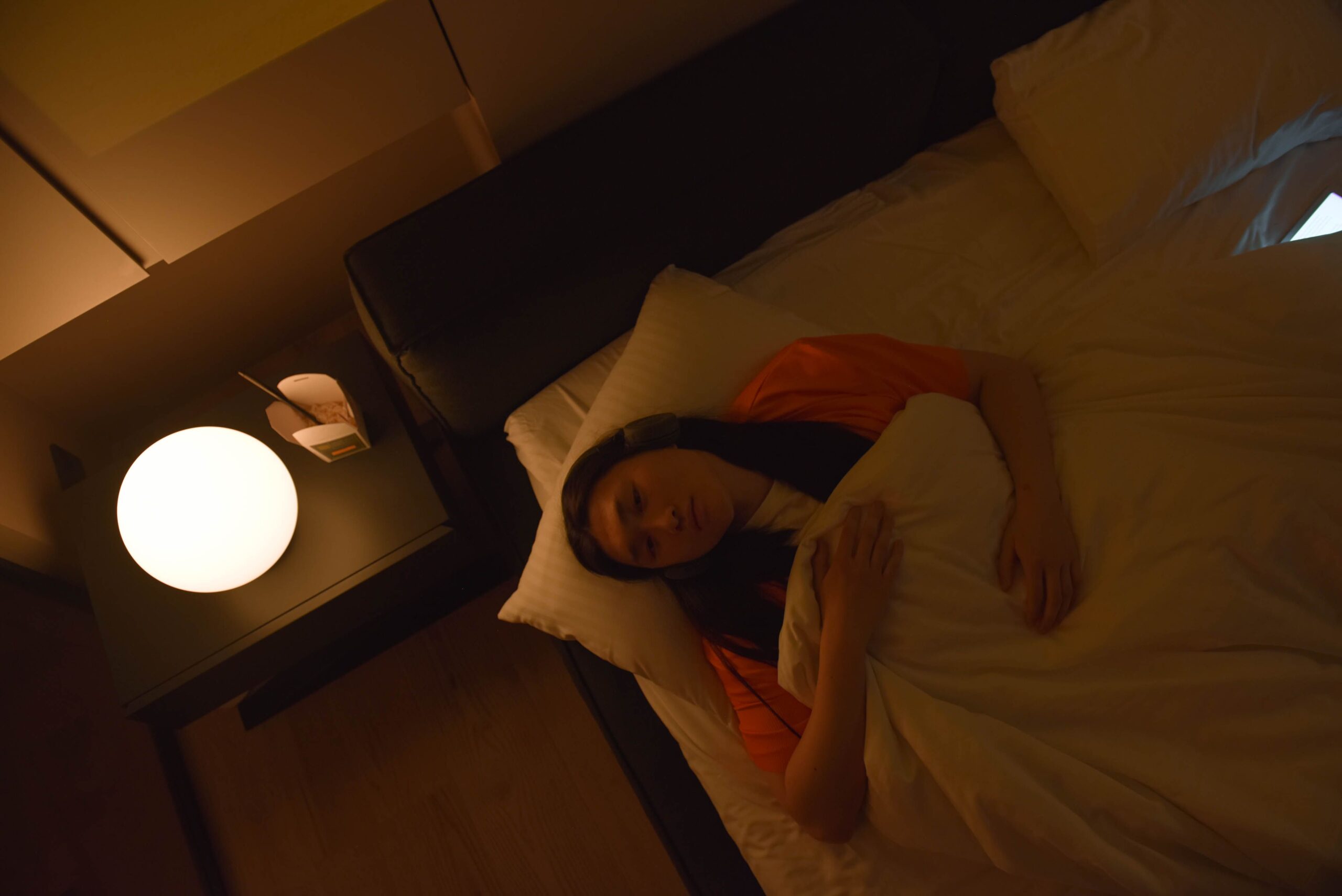 Mulher deitada na cama de olhos abertos, vista de cima, sem conseguir dormir