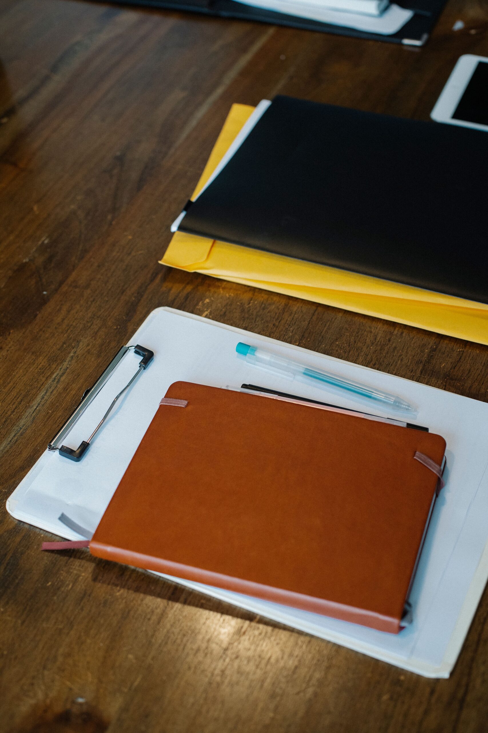 Caderno, prancheta com papéis, pastas e canetas sobre uma mesa