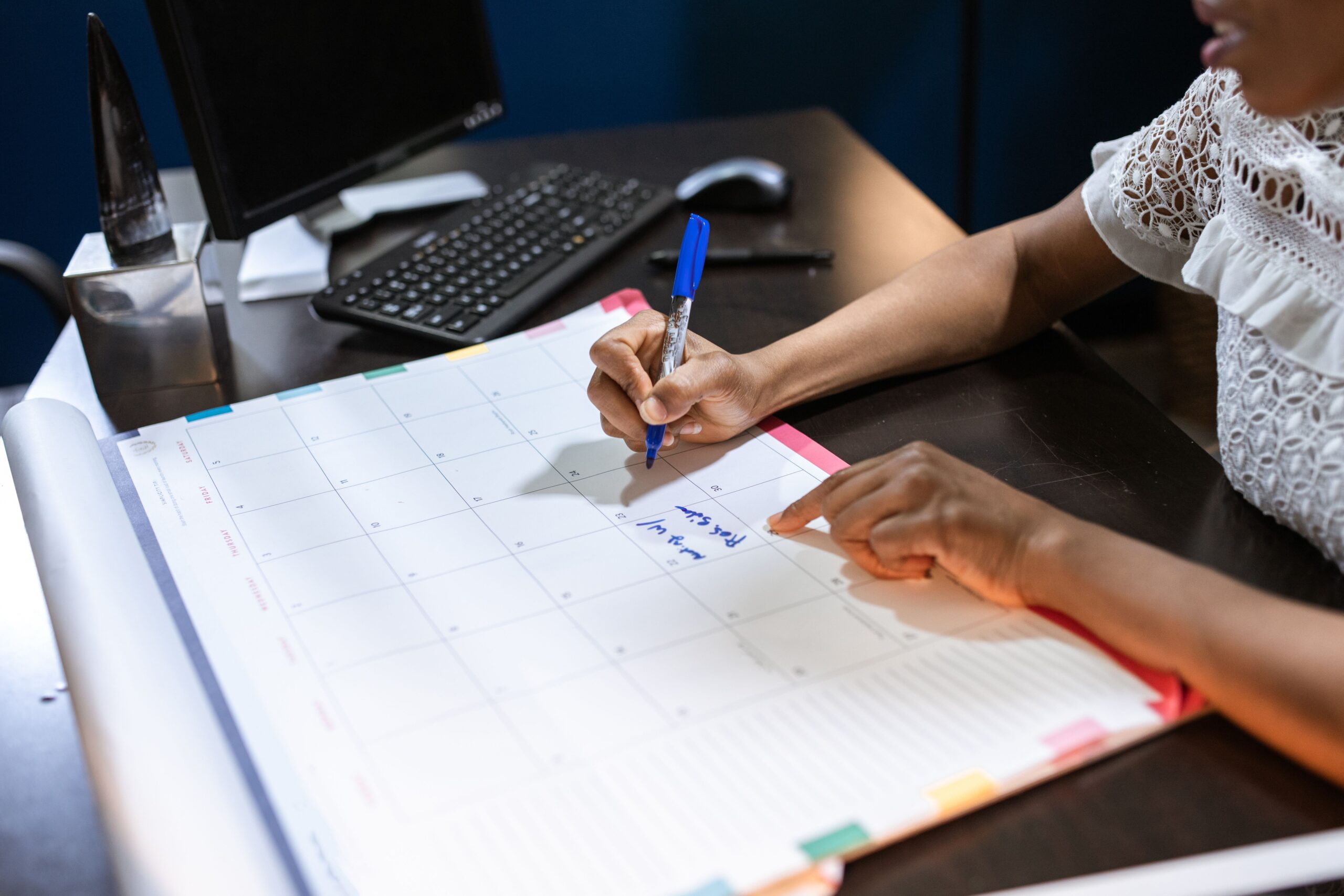 Pessoa escrevendo compromissos em um calendário de mesa