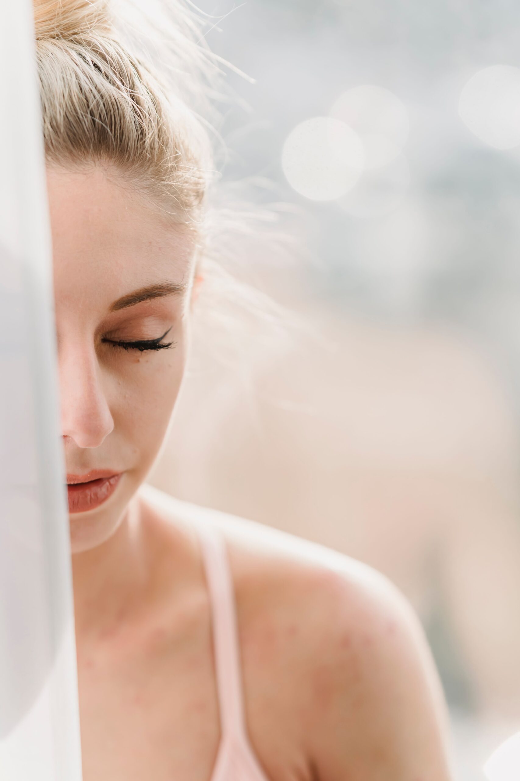 Mulher de olhos fechados respirando com calma perto da janela