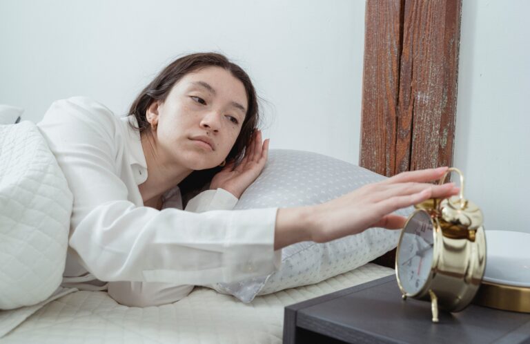Mulher estendendo o braço para desligar o despertador na cama