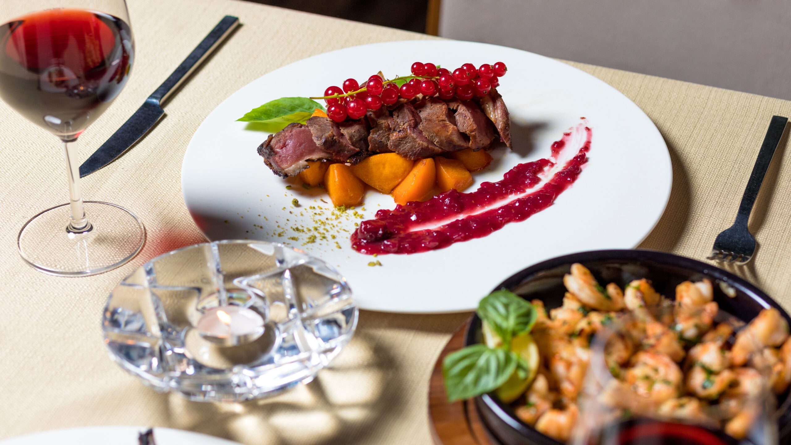 Prato com carne, acompanhamentos e talheres sobre mesa de madeira